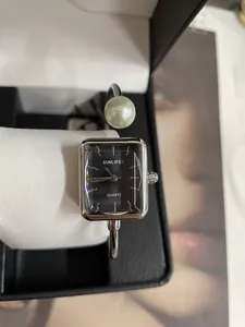 Primo piano di un orologio al quarzo quadrato con perla decorativa su cinturino in metallo