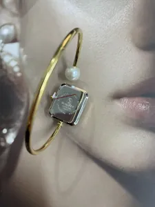 Primo piano dell'orologio rigido quadrato dorato con perla e retro in acciaio.