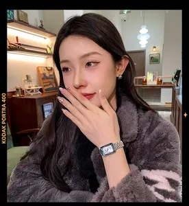 Detailed close-up of a stylish silver rectangular watch worn by a model in a cafe.
