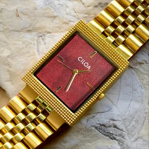 Gros plan détaillé d'une montre pour homme CILOA rétro carrée en or avec cadran rouge.