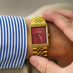 Gros plan d'une montre carrée dorée vintage CILOA avec cadran rouge texturé au poignet