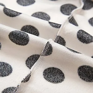 Détail en gros plan d'un tissu blanc à pois noirs montrant la texture des coutures