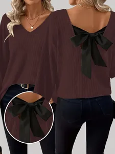 Detalle de un suéter de punto marrón con cuello en V para mujer y un lazo negro grande en la espalda