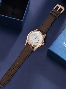 Elegantes Detail der TOMI Modeuhr mit braunem Lederarmband und roségoldenem Gehäuse auf Blau.