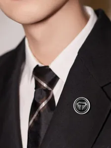 Detailed view of a TOMI men's silver and black round lapel brooch on a black suit jacket