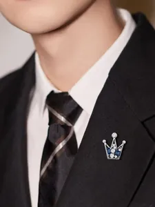 Détail d'une élégante broche couronne en argent avec pierres bleues et blanches sur costume