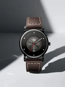 Dettaglio dell'orologio minimalista TOMI con datario e cinturino in pelle marrone.