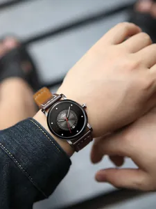 Primo piano dell'orologio minimalista TOMI con cinturino in pelle marrone e datario al polso.