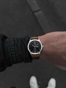 Close-up detail of a TOMI watch face and brown leather strap worn on a male wrist