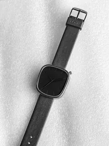 Vue détaillée de la montre quartz TOMI noire avec bracelet en cuir sur fond texturé