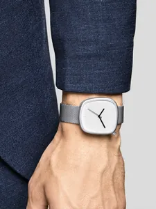 Détail d'une montre à quartz minimaliste en forme de galet avec un bracelet en maille.