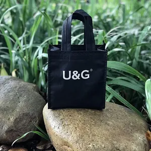 Una piccola borsa regalo nera firmata U&G esposta su una base di roccia naturale.