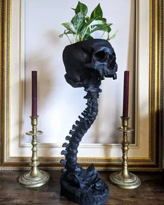 Jardinière tête de mort noire gothique avec support colonne vertébrale et chandeliers.