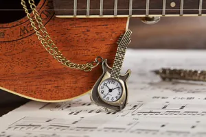 Vintage bronze guitar-shaped pocket watch with chain on musical sheet