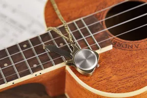 Detailed close-up view of vintage bronze guitar-shaped pocket watch pendant on ukulele