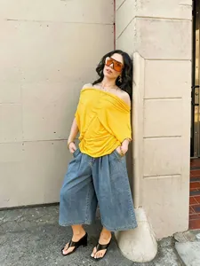 Urbaner Streetstyle Frau in weiter Denim-Culotte und gelbem schulterfreiem Top