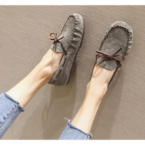 Nahaufnahme von grauen Wildleder-Mokassins mit brauner Lederschleife zu blauen Jeans.