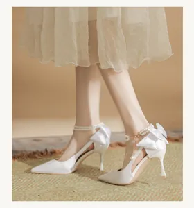 Detail view of white bridal high heels featuring a large satin bow and pearl ankle strap