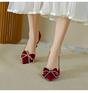 Dettaglio di décolleté in raso bordeaux con fiocco di strass e punta affusolata.