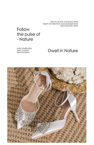 Close-up of white satin pointed-toe stiletto heels with rhinestone flower decoration.