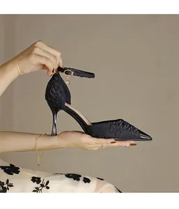 Close-up of black pointed-toe high heels with textured fabric and gold ankle strap charm