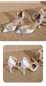 Elegant pointed-toe white satin high heels featuring a sparkling rhinestone bow detail.