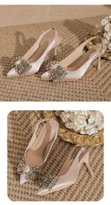 Detail view of champagne satin pointed-toe stiletto heels with crystal flower adornment.