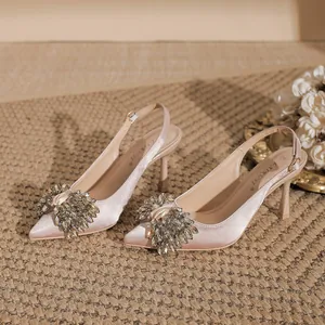 Elegant champagne satin pointed-toe heels with sparkling rhinestone bow detail.