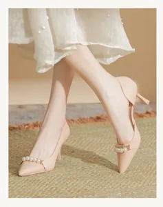 Detailed close-up of elegant nude pointed-toe high heels featuring pearl straps on model