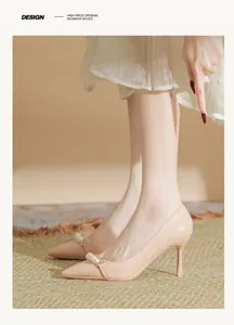 Detail of beige pointed-toe heels with pearl and chain accents on feet