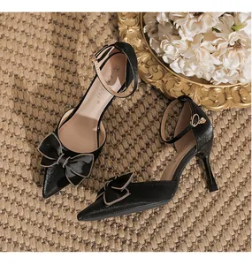 Detailansicht eleganter schwarzer Pumps mit spitzer Kappe und goldverzierter Schleife.