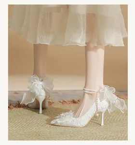 Elegant close-up of white lace wedding stilettos featuring pearl straps and large mesh bows