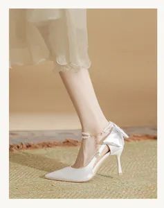 Close-up of white bridal high heels with pearl anklet and heel bow detail