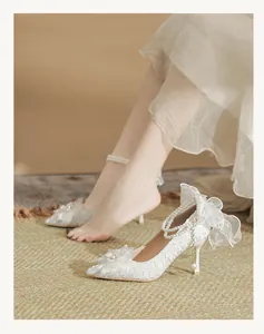 Detail of white lace wedding shoes featuring elegant pearl chains and a large tulle bow