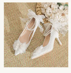 Detailed view of elegant white bridal high heels with lace, pearls, and a large mesh bow.