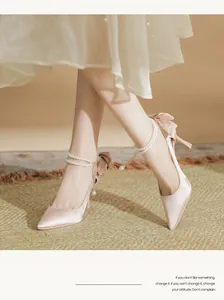 Close-up of champagne satin bridal high heels with pearl straps and bow details.