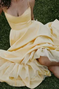 Elegant close-up of yellow French corset dress with layered mesh ruffle hem on green grass
