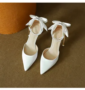 Close-up detail of elegant white pointed toe high heels with silk bows and pearl ankle straps