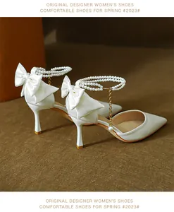 Detail view of white satin pointed-toe heels featuring a back bow and pearl ankle strap