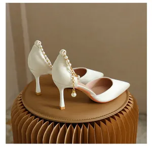 Detail von cremefarbenen Stiletto-Pumps mit eleganter Perlenkette am Knöchel