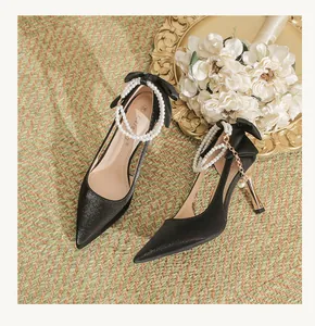 Elegant black pointed high heels with pearl ankle straps and bow detail in wedding setting.
