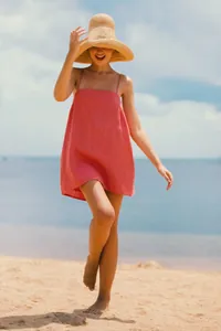 Mannequin portant une robe bohème en lin rose corail sur une plage ensoleillée d'été