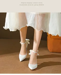 Detailaufnahme von weißen Seidenpumps mit spitzer Kappe und eleganten Knöchelriemenschleifen