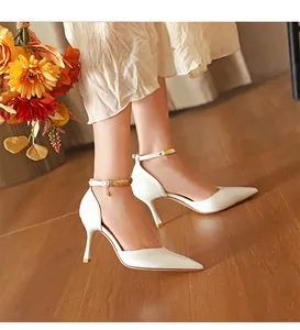 Elegante weiße spitze Pumps mit goldenem Anhänger am Knöchelriemen, am Bein getragen