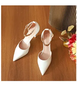 Elegante weiße Pumps mit spitzer Kappe und Metallketten-Knöchelriemen auf Holztisch.