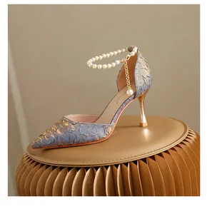 Close-up of blue jacquard pointed-toe pumps with elegant pearl ankle strap and gold stiletto heel.