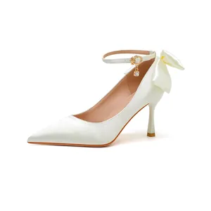 Detailansicht der weißen Satin-Pumps mit Fesselriemen und dekorativer Schleife an der Ferse