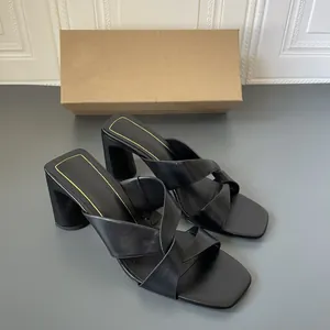 Dettaglio di eleganti sandali neri con tacco largo, cinturini incrociati e bordo oro