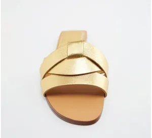 Dettaglio macro dei cinturini incrociati metallizzati dorati su un sandalo piatto a punta quadra.