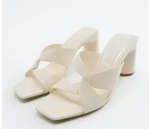 Dettaglio di sandali beige con tacco a blocco, eleganti cinturini incrociati e punta quadra.